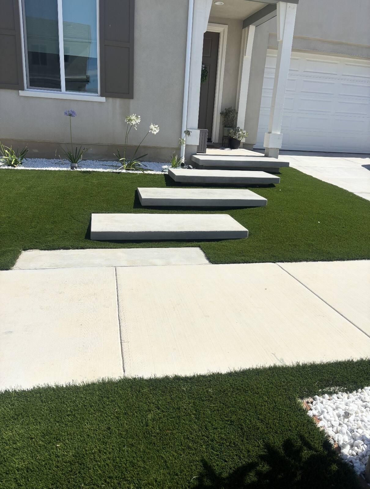 Floating concrete pads set into artificial turf, stepping from a concrete walkway toward a front entry